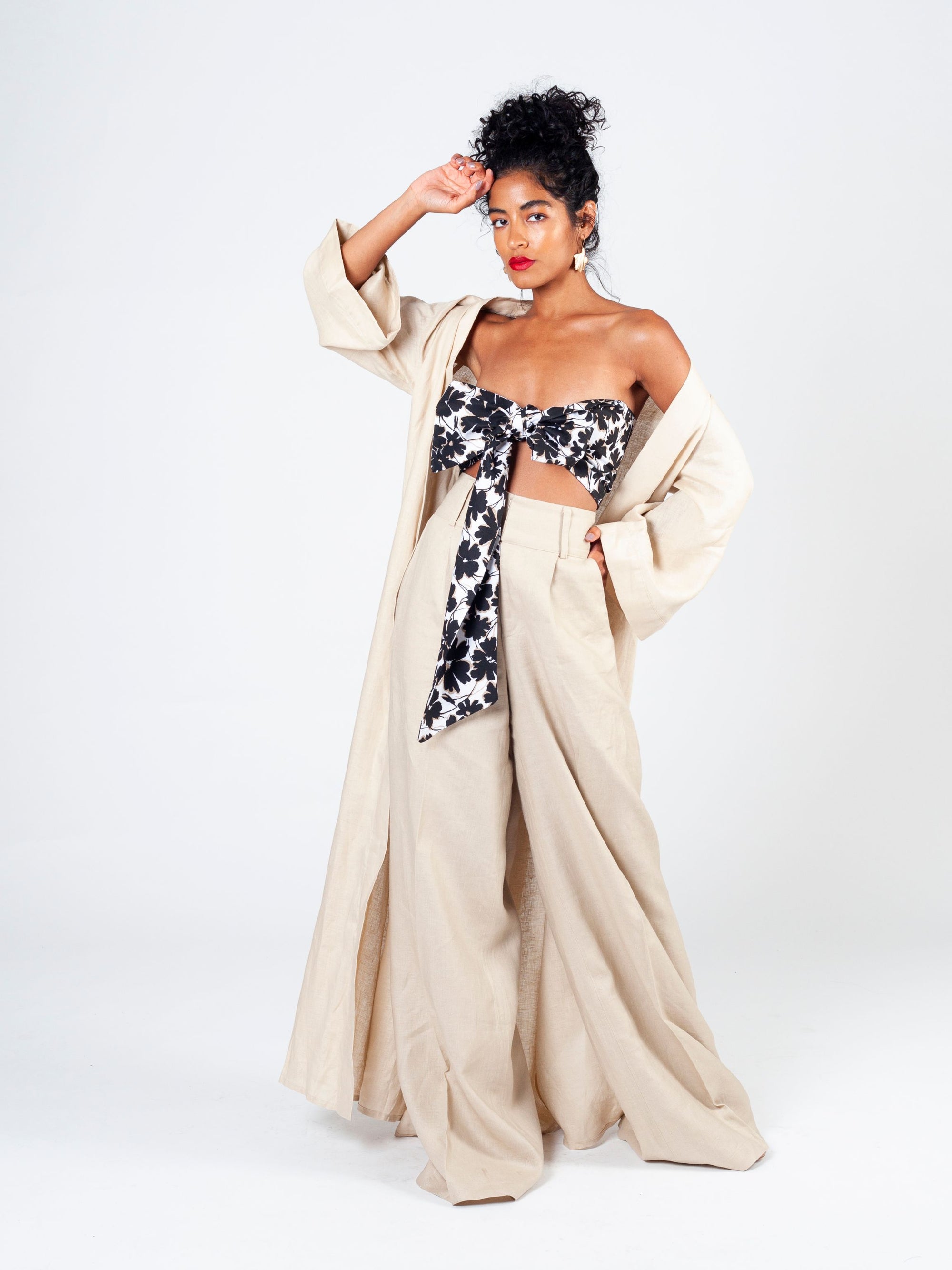 Model in a long, open-front duster made from soft natural-toned linen. The duster has wide sleeves and a relaxed fit, worn over a matching linen trouser and bandeau top set.