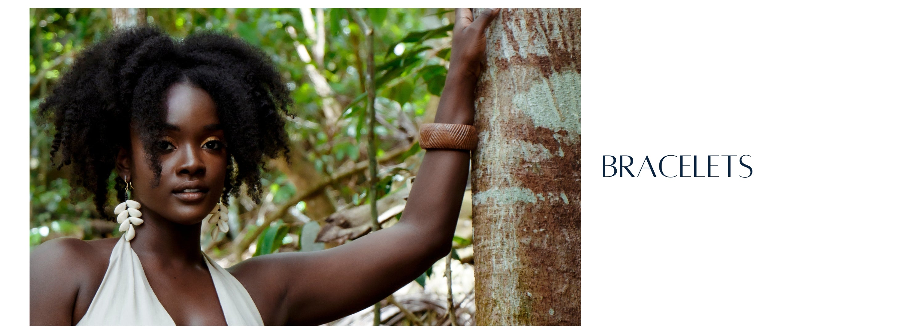 Woman standing in rainforest in Antigua, resting her hand on a tree wearing brown wooden bangle.