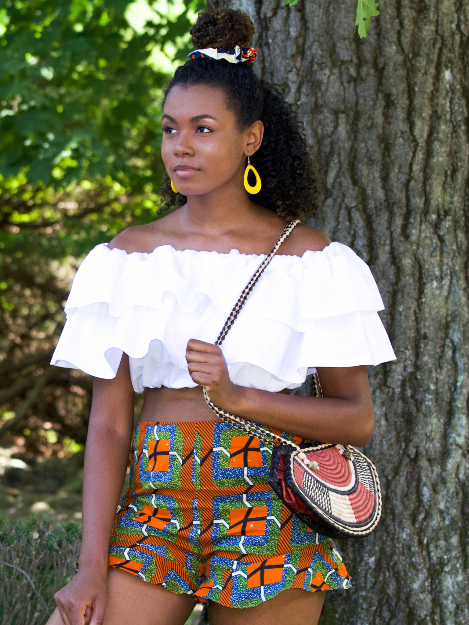 Black model wears high waist shorts with frilled hem. Patter on shorts is a mixture of stripes and squares in orange, black, white, blue and green colours.