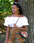 Black model wears high waist shorts with frilled hem. Patter on shorts is a mixture of stripes and squares in orange, black, white, blue and green colours.
